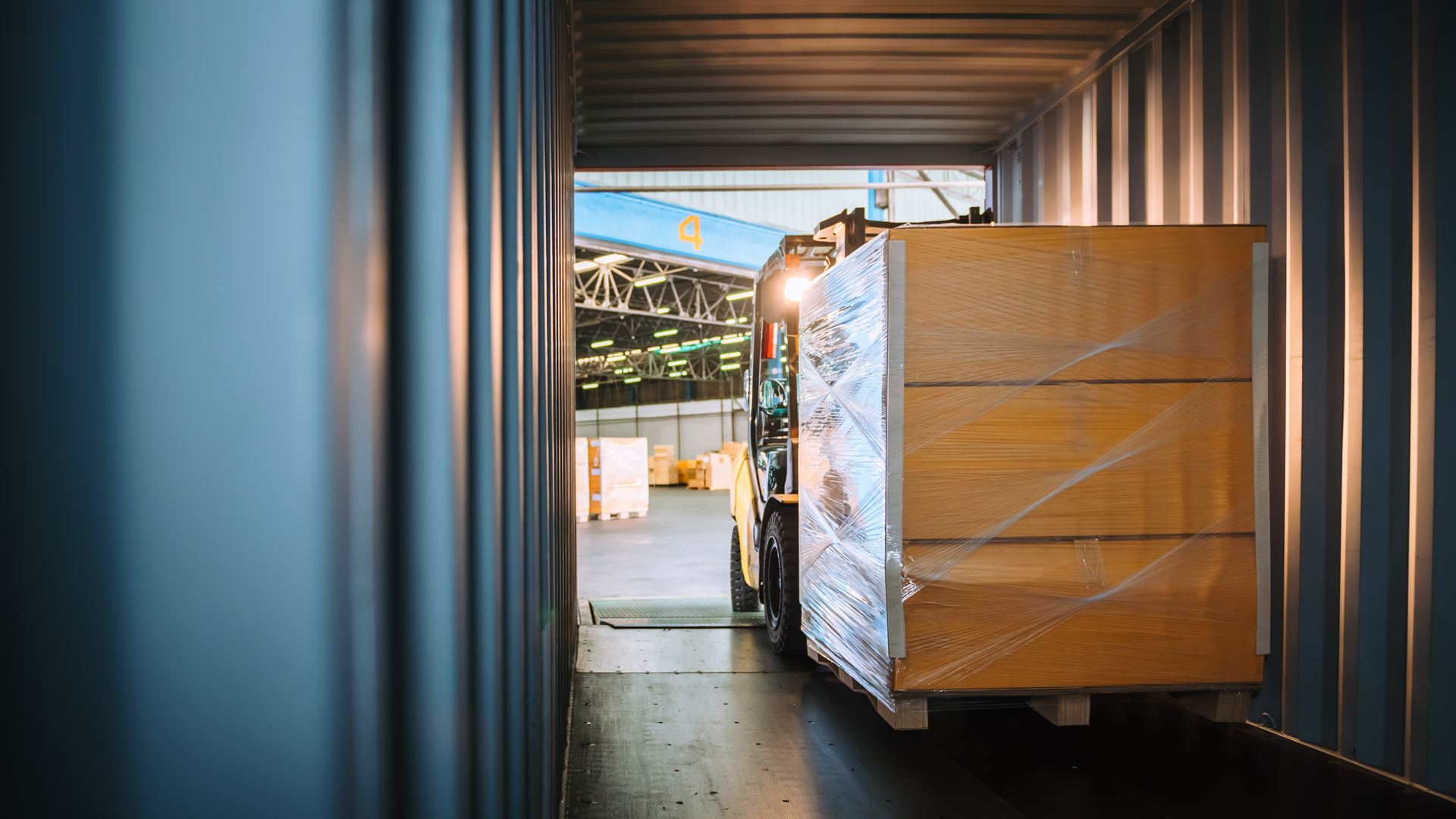 Forklift loading shrink-wrapped pallets into a shipping container at a warehouse dock