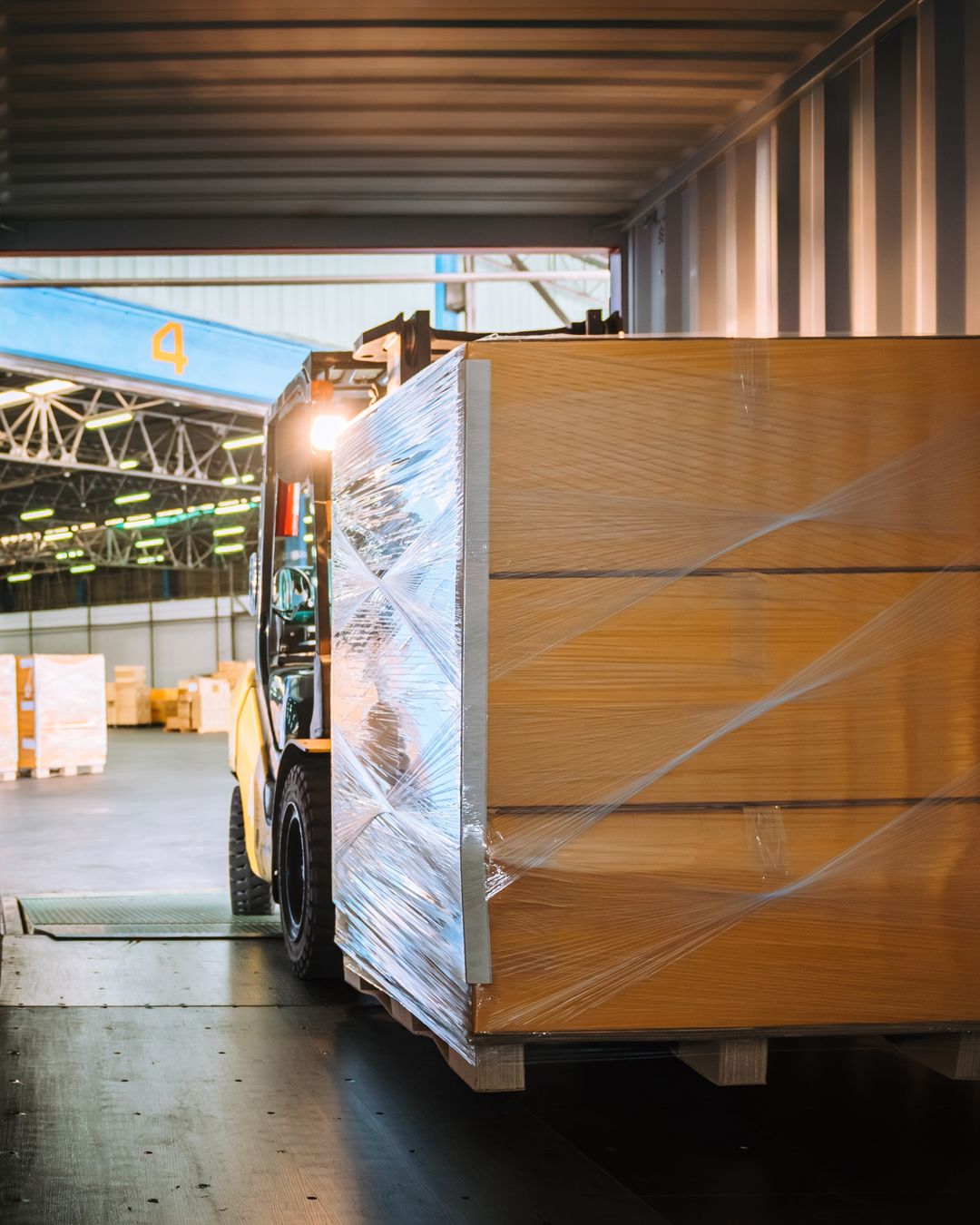 Forklift loading shrink-wrapped pallets into a shipping container at a warehouse dock