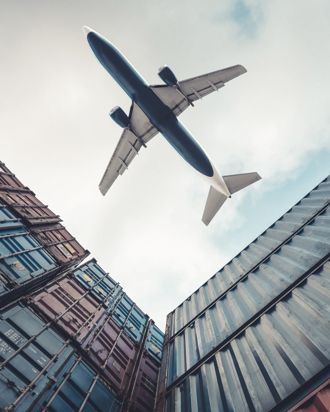 Cargo plane flying over stacked shipping containers