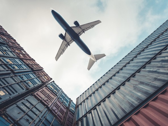 Cargo plane flying overhead between stacked shipping containers