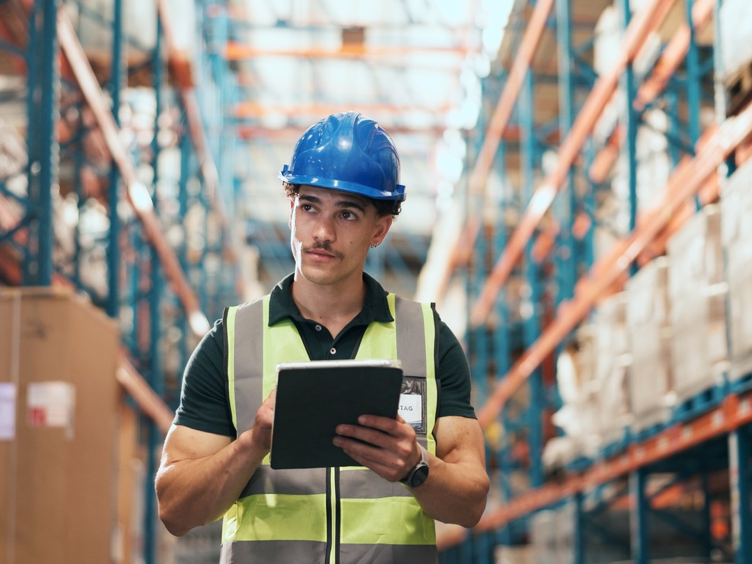 Warehouse worker in a hard hat checking inventory on a tablet